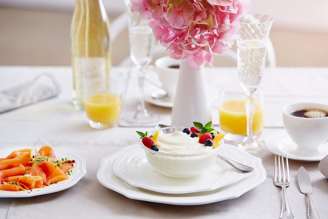 A breakfast table with yoghurt, salmon, coffee, Prosecco and orange juice