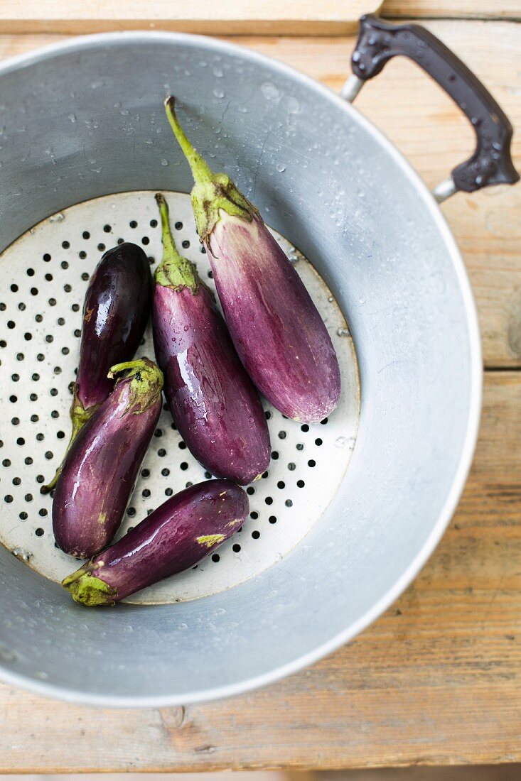 Freshly washed aubergines in a colander