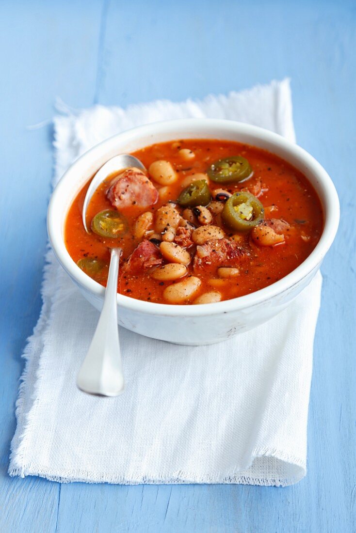 A stew with tomatoes, jalapeños, smoked pork belly, sausages and beans