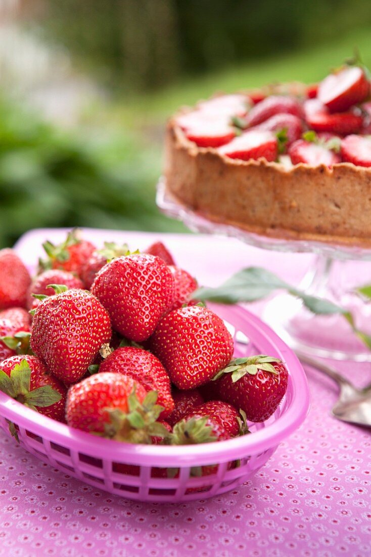 A basket of fresh strawberries with a strawberry cake in the background