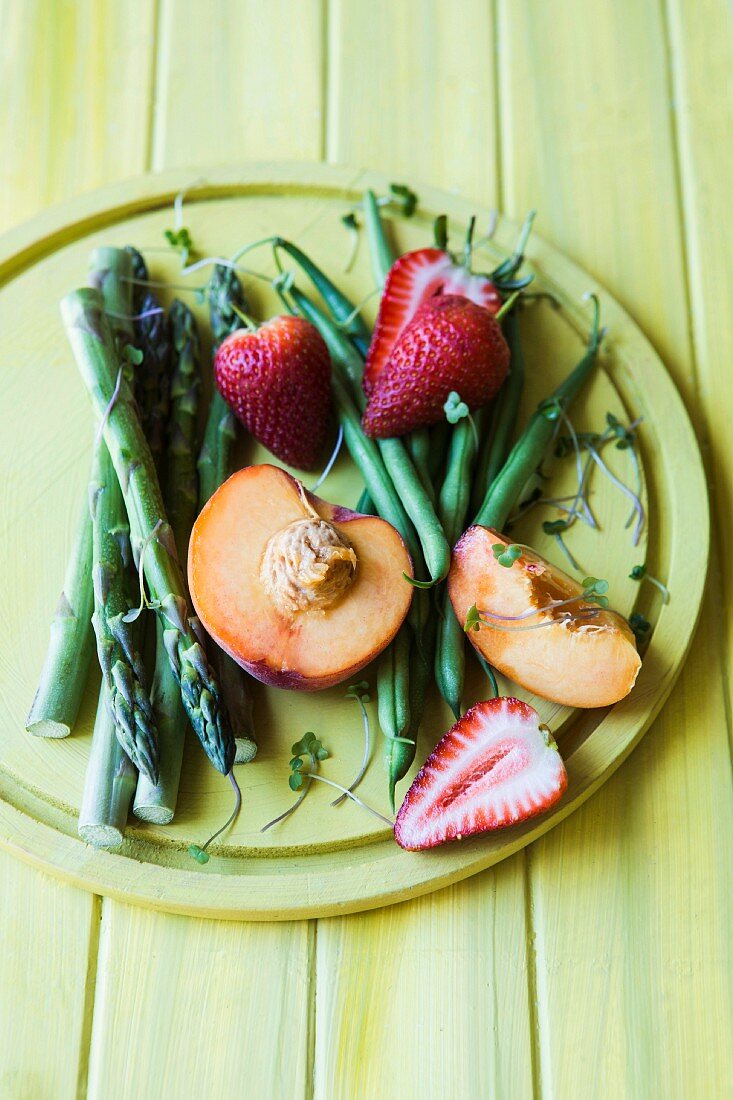 An arrangement of green asparagus and green beans, strawberries and peaches