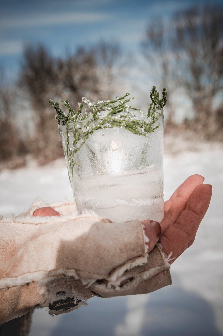 Candle lantern made from ice and twigs held in hand wearing fingerless glove