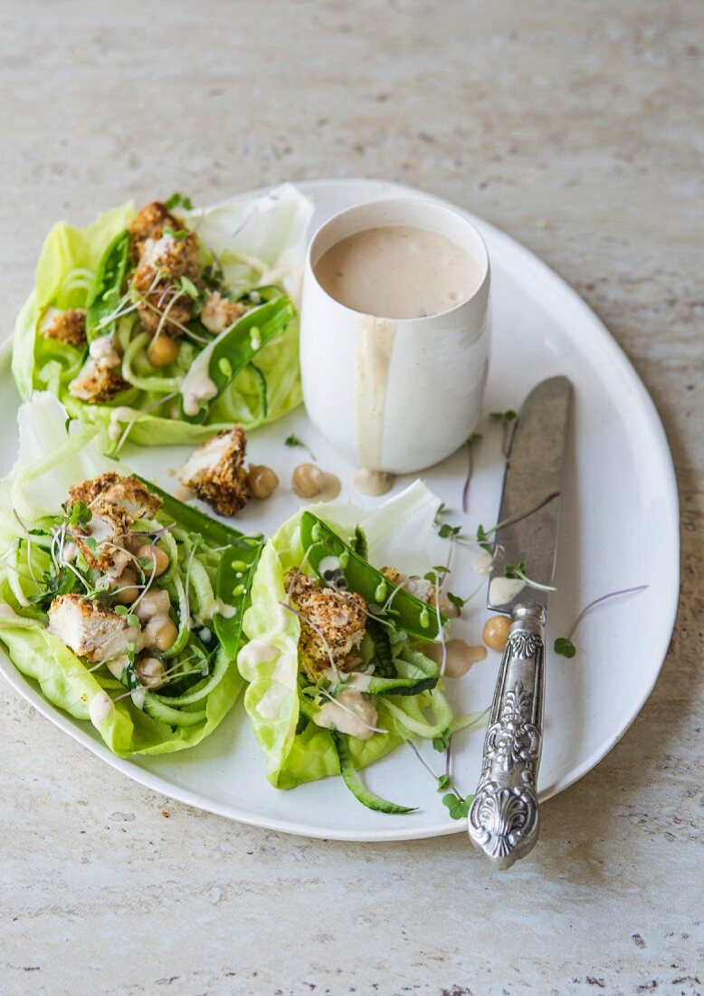 Chicken with a bread crust and vegetables in lettuce leaves served with coconut and peanut butter