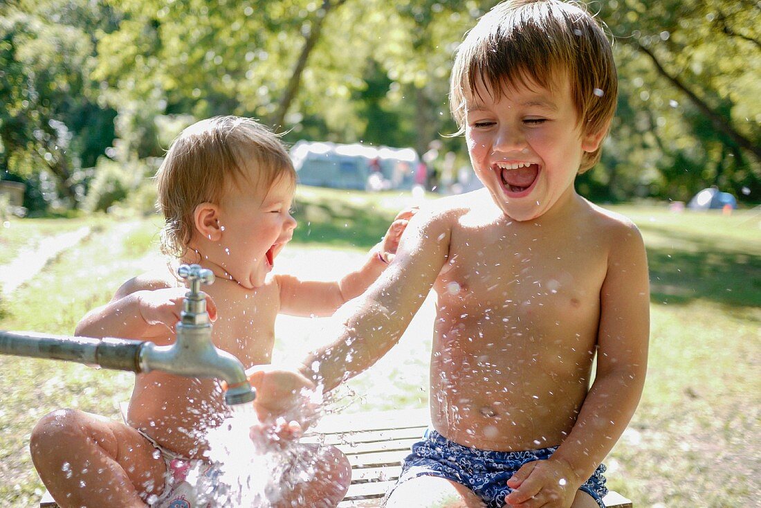 Kleiner Junge und kleine Schwester spielen mit Wasser im Garten