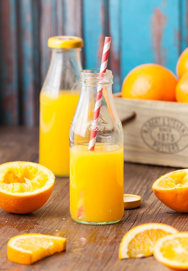 Two bottles of freshly pressed orange juice surrounded by oranges