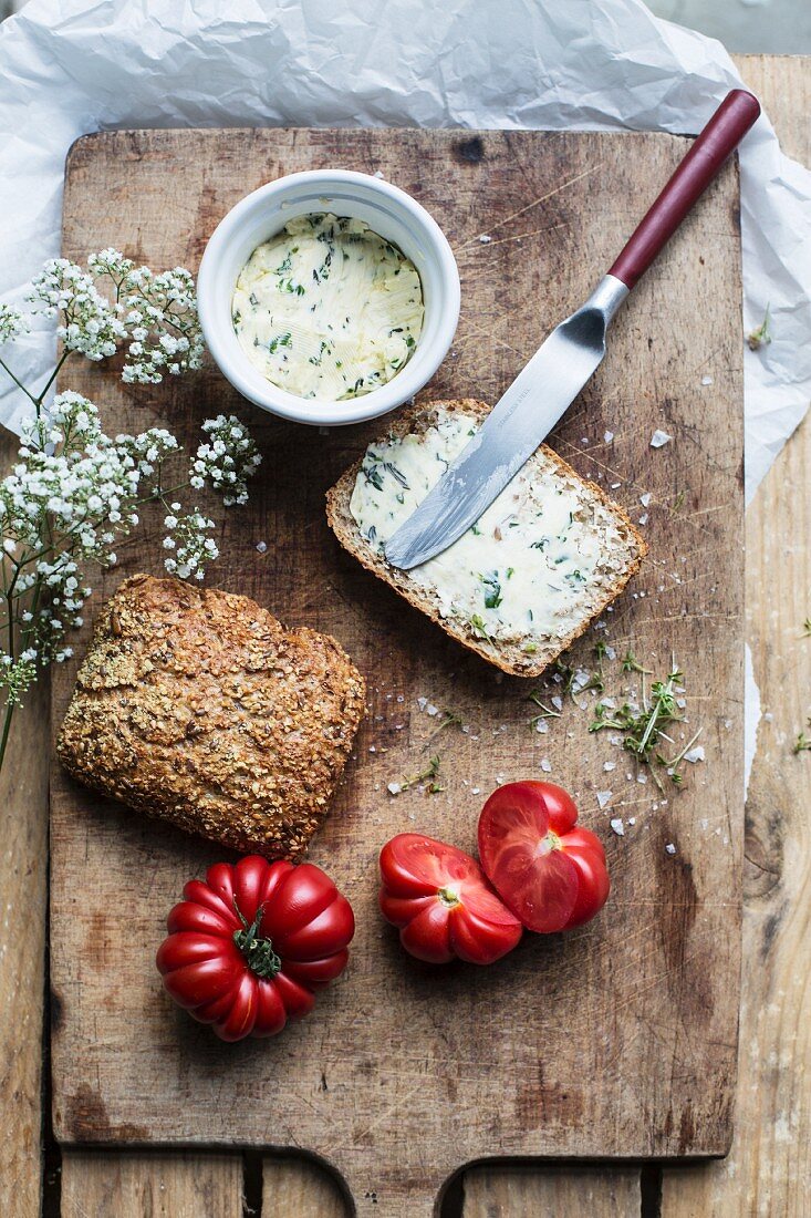 Brot mit Kräuterbutter und Tomaten auf altem Schneidebrett