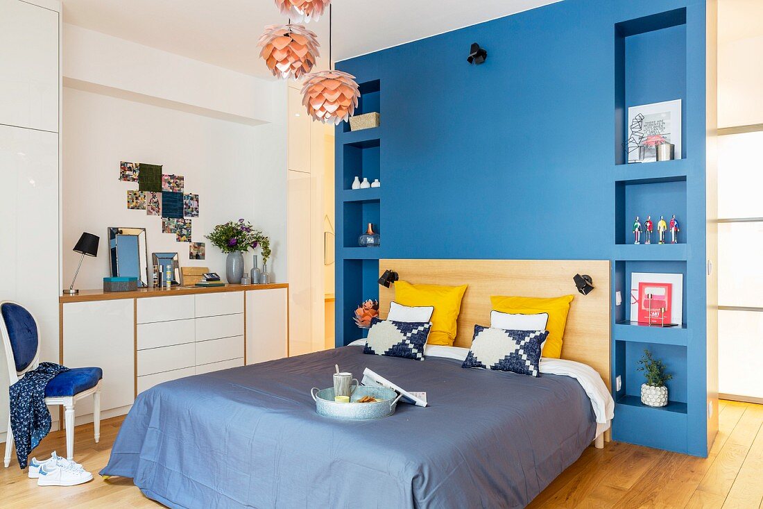 Bett an blauer Wand mit Einbauregalen zu beiden Seiten