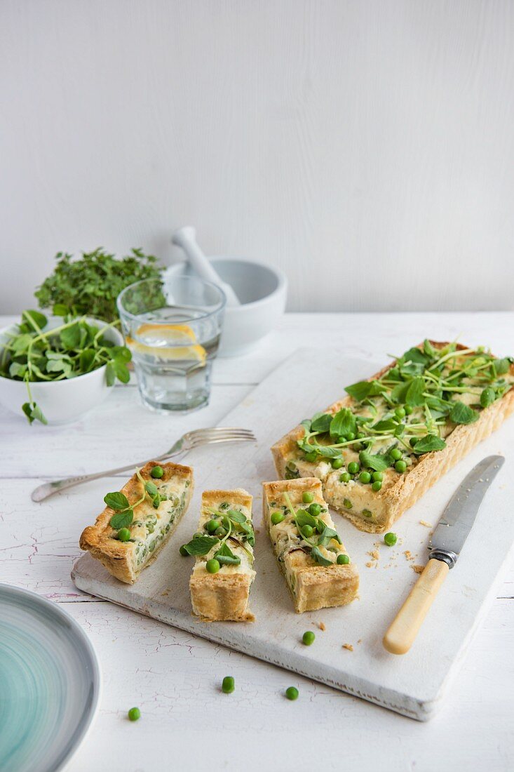 A tart topped with peas, cheese and pea shoots, sliced