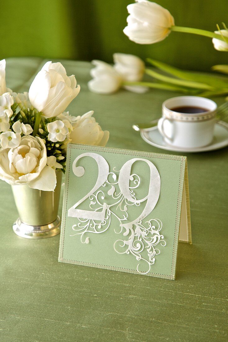 Dekoratives Kärtchen mit der Zahl 29 neben weißem Blumensträusschen auf festlichem Tisch