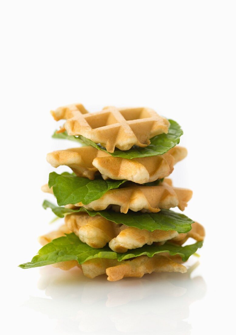 A stack of vegan waffles with lettuce leaves on a white surface