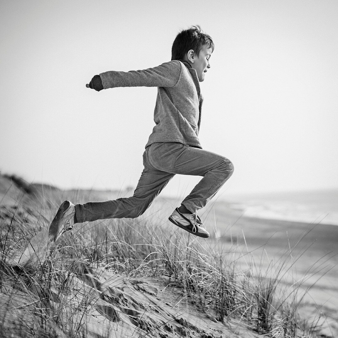 A little boy jumping from sanddunes (black-and-white shot)