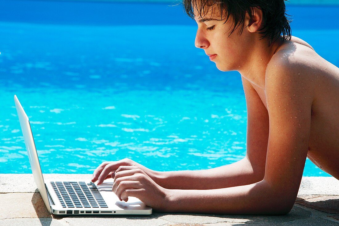 Teenager using a laptop by a pool