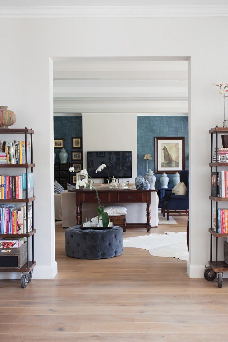 View through wide, open doorway into living room with grey pouffe on continuous wooden floor