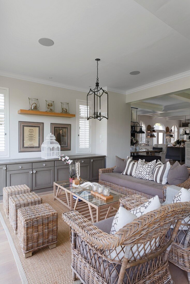 Lounge area with rattan furniture, delicate coffee table and grey-painted sideboard in open-plan interior