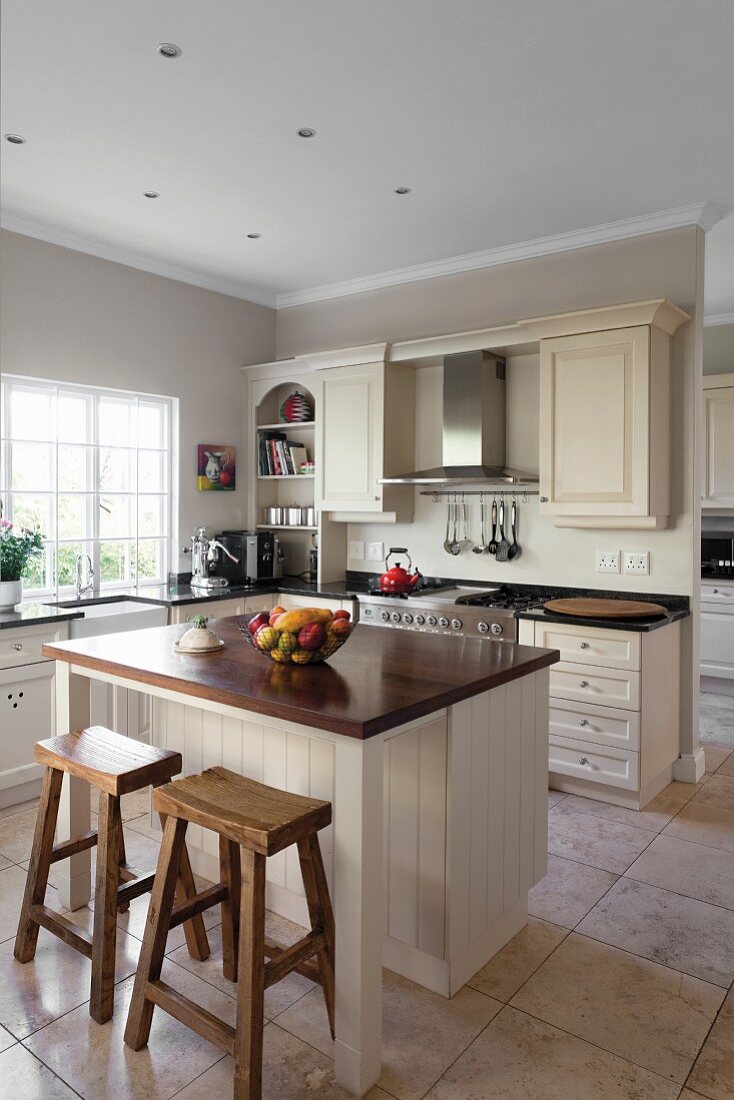 Pale country-house-style kitchen with free-standing counter and rustic bar stools