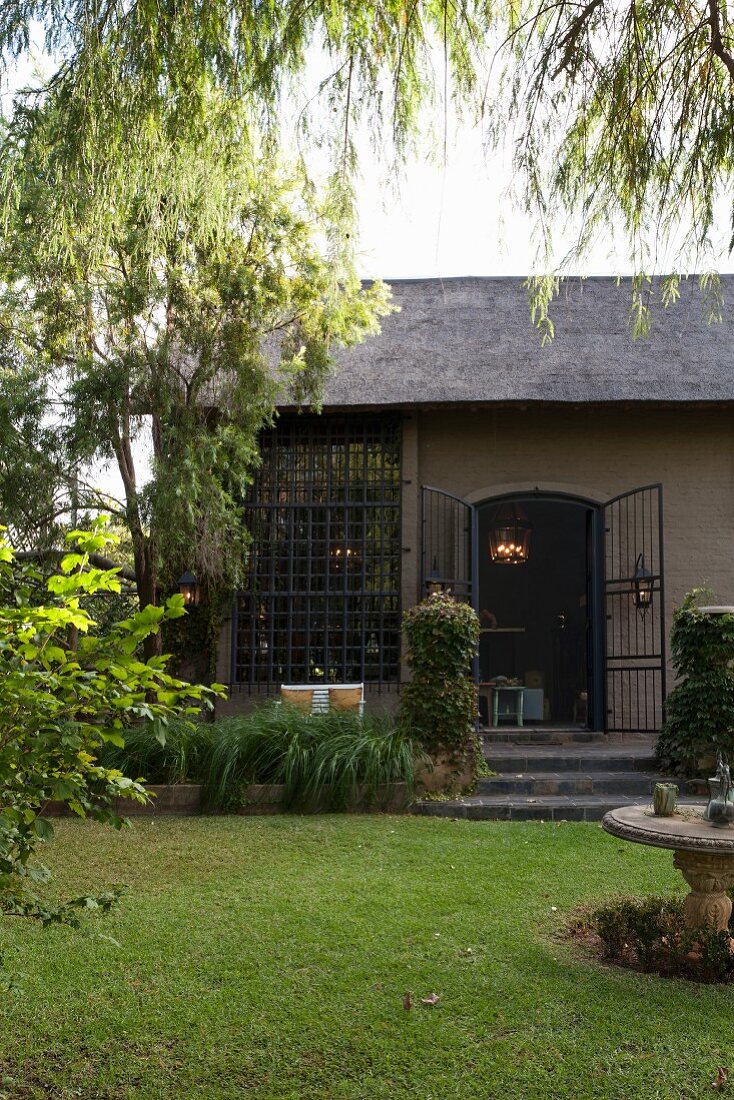 Blick vom Garten auf umgebaute Scheune mit vergittertem raumhohem Fenster und offener Metallgitter Tür