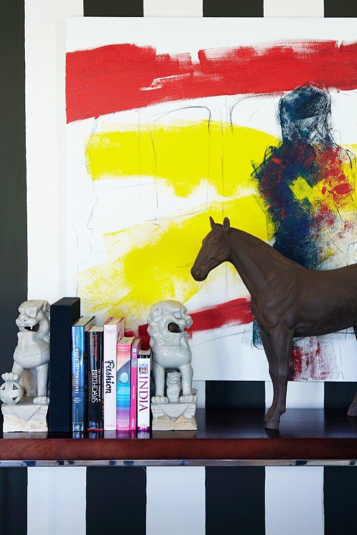 Various china and metal animal ornaments on shelf below modern artwork