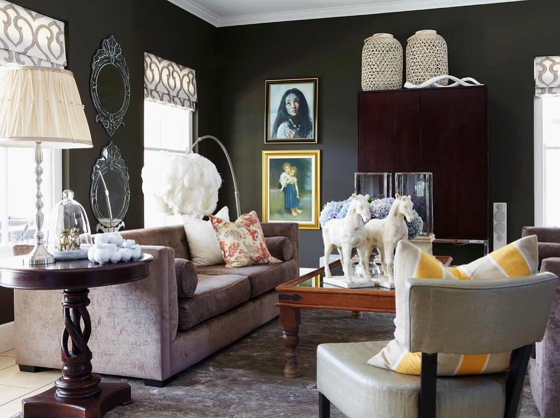 Lounge area with armchair, round, dark wood side table and table lamp next to sofa in black-painted living room