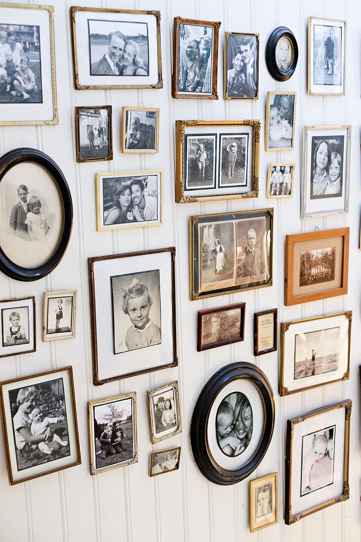 Gallery of retro-style family photos in various frames on white wooden wall