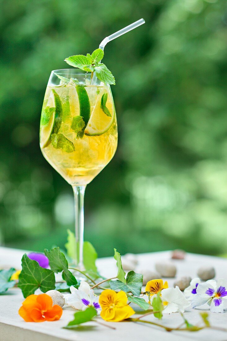A glass of lemonade made with limes, mint and edible flowers on a garden table