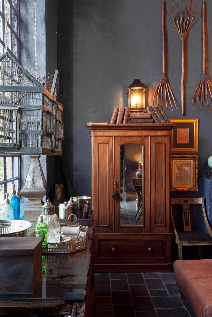 Antique wooden wardrobe in corner below wooden pitchforks hung on black-painted wall