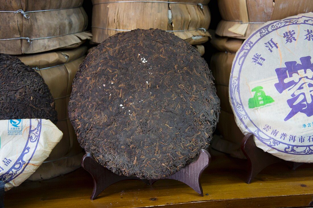 Zu Fladen gepresster Pu-Erh-Tee, teilweise verpackt in Verkaufsregal (Lijiang, China)