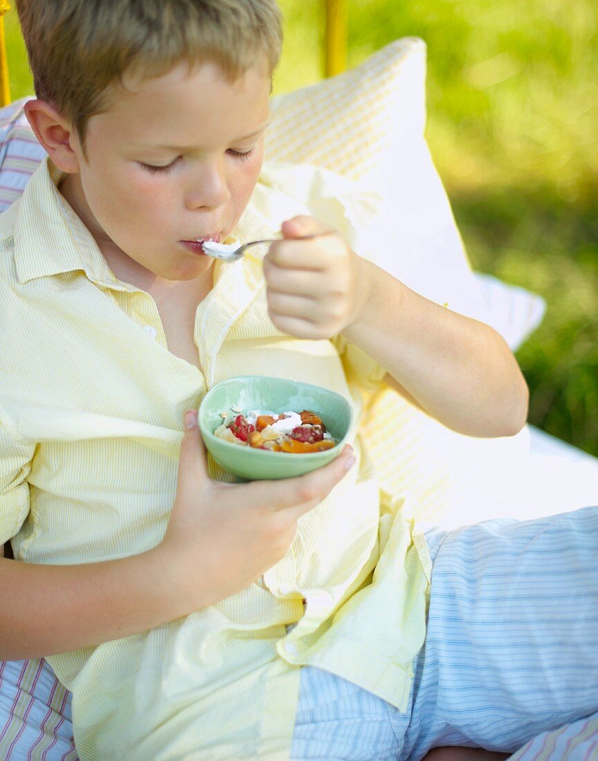 A boy eating muesli for breakfast in bed in a field