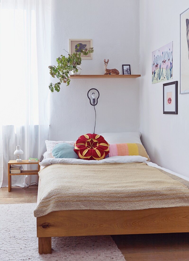 Bett mit beigefarbener Tagesdecke und Kissen in Blütenform in Zimmerecke