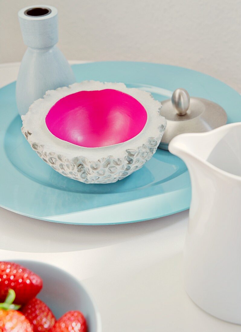 Betonschale - innen Magenta - mit Vase auf hellblauem Porzellanteller; Milchkännchen und Erdbeerschale im Vordergrund