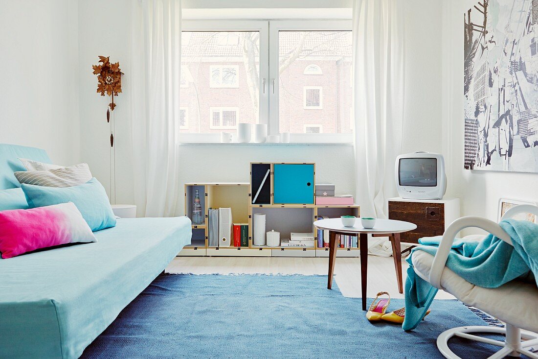 Youthful interior in shades of blue with scatter cushions on sofa bed, cuckoo clock and delicate designer furniture