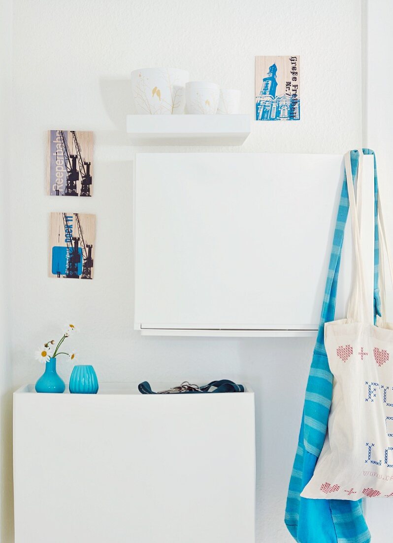 Blaue, dänische Vasen auf weißem Schuhregal und künstlerische Postkarten an der Wand