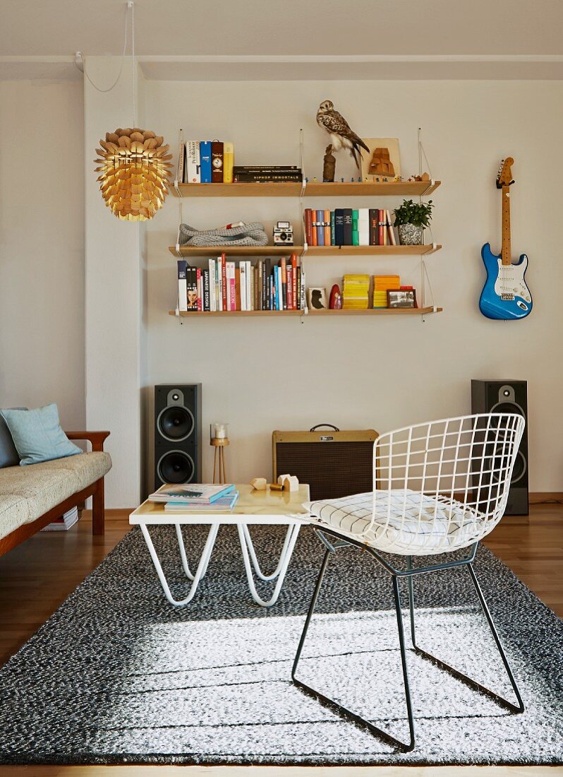 Klassiker Maschendraht Stuhl und Couchtisch auf Teppich, an Wand gegenüber aufgehängtes Regal und Gitarre