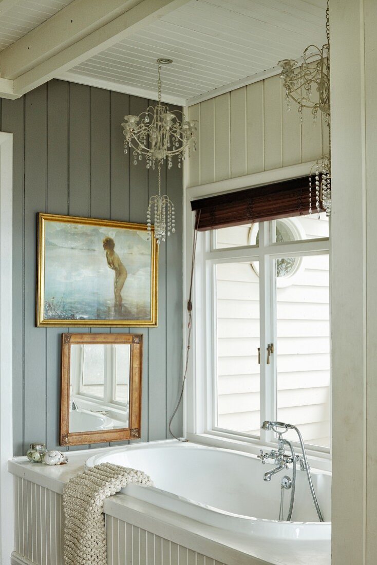 Holzverkleidetes Bad, Kerzenleuchter an Decke über eingebauter Badewanne, an grauer Holzwand Bilder mit Goldrahmen