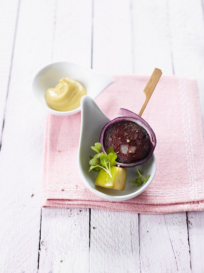 Blood sausage wrapped in onion on a stick with a piece of apple