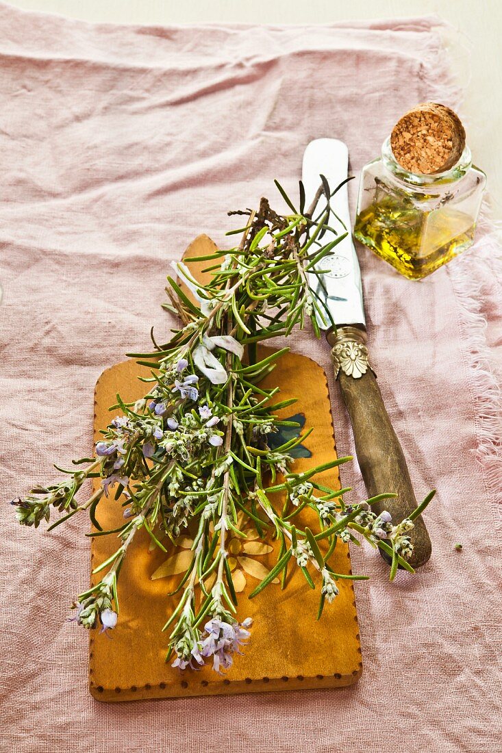 Rosemary oil in front of flowering rosemary on a wooden board