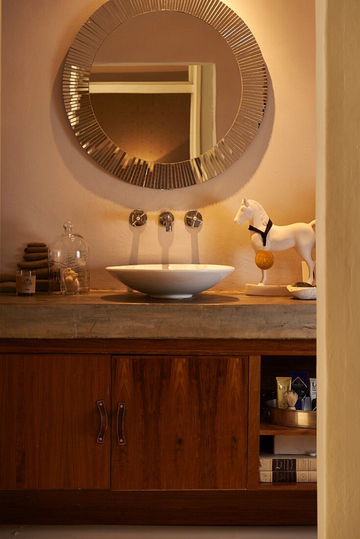 Eingebauter Waschtisch mit Schüssel auf Betonplatte und Holz Unterschrank, an Wand runder Spiegel mit Rand