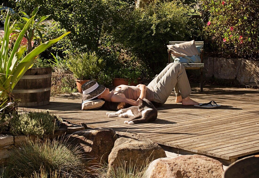 Sunny spot for relaxing in garden - woman and cat lying on wooden deck