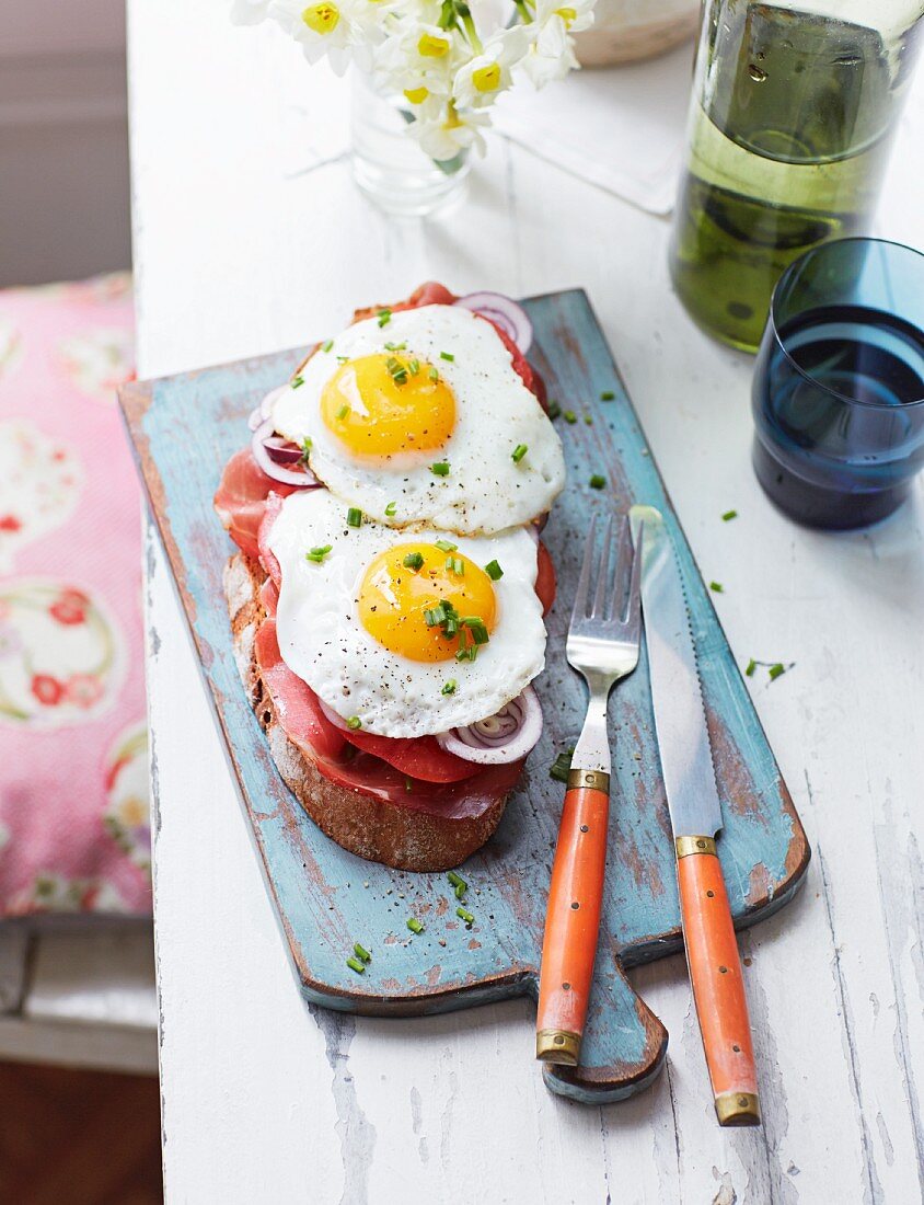 A slice of bread topped with tomato, bacon and fried eggs