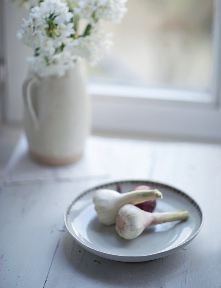 Stillleben mit Knoblauch & Zwiebel auf Teller dahinter Blumen in Vase