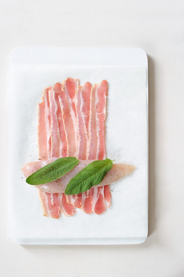 A raw chickens breast with sage leaves on bacon rashers