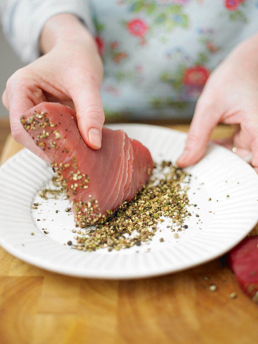 Tuna fish steak being coated in peppercorns