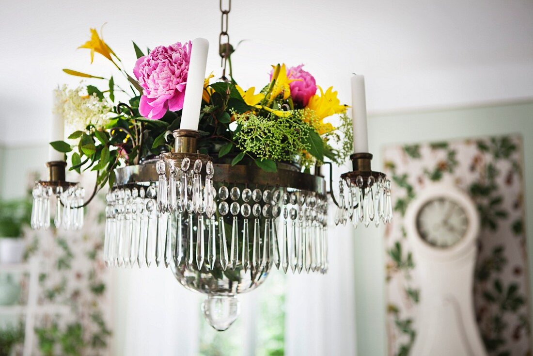 Summer flowers on chandelier with glass droplets and white candles suspended from ceiling