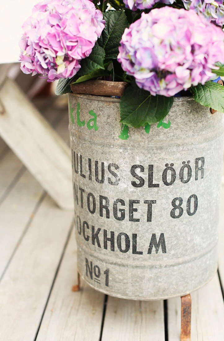 Purple hydrangeas in zinc bucket with lettering on rustic wooden terrace