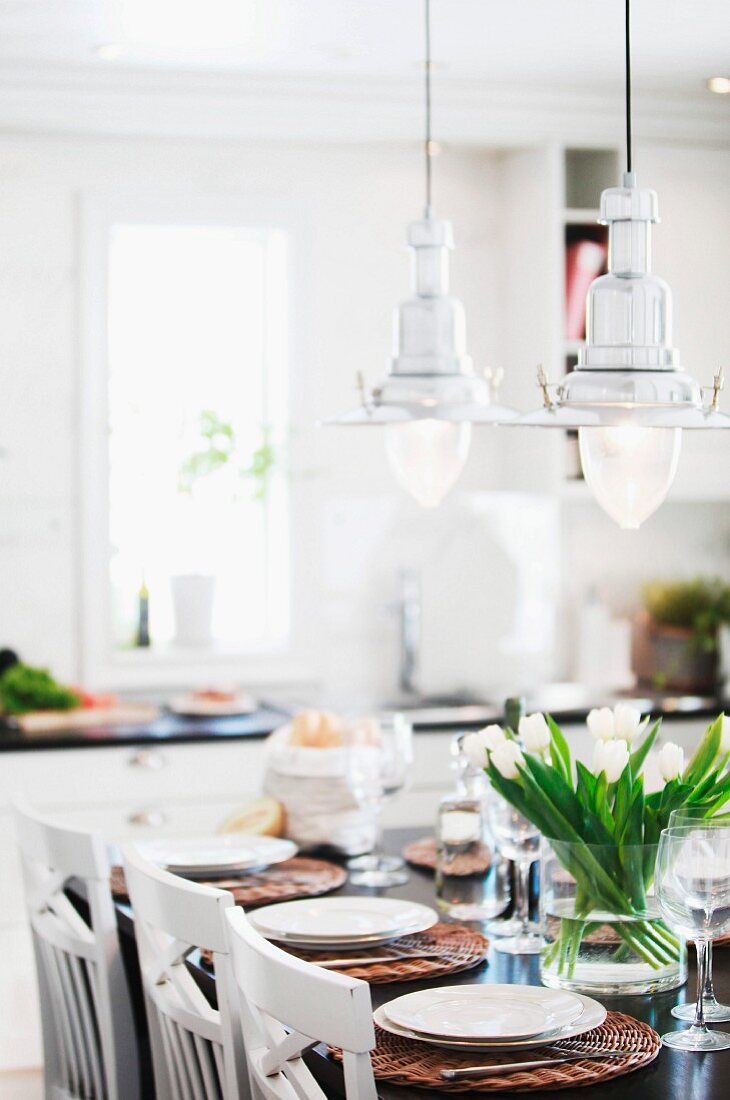 Pendelleuchten im maritimen Retrostil und festlich gedeckter Tisch mit Tulpenstrauss im Ambiente einer weissen, skandinavischen Küche
