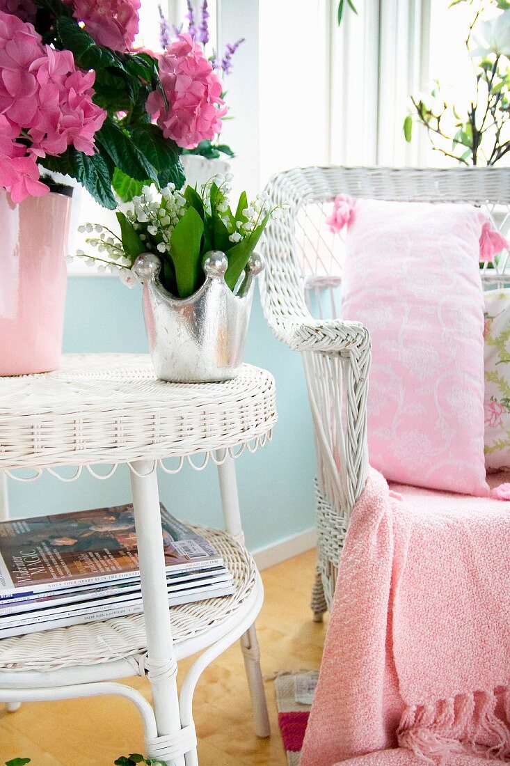 Vase of flowers on white wicker side table next to matching armchair with pink patterned cushions