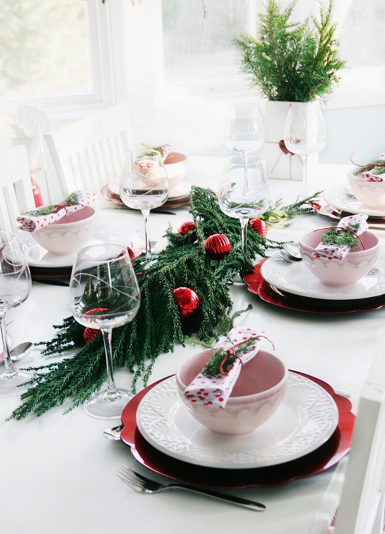 Table set for restive lunch with conifer branches and red Christmas baubles arranged in centre