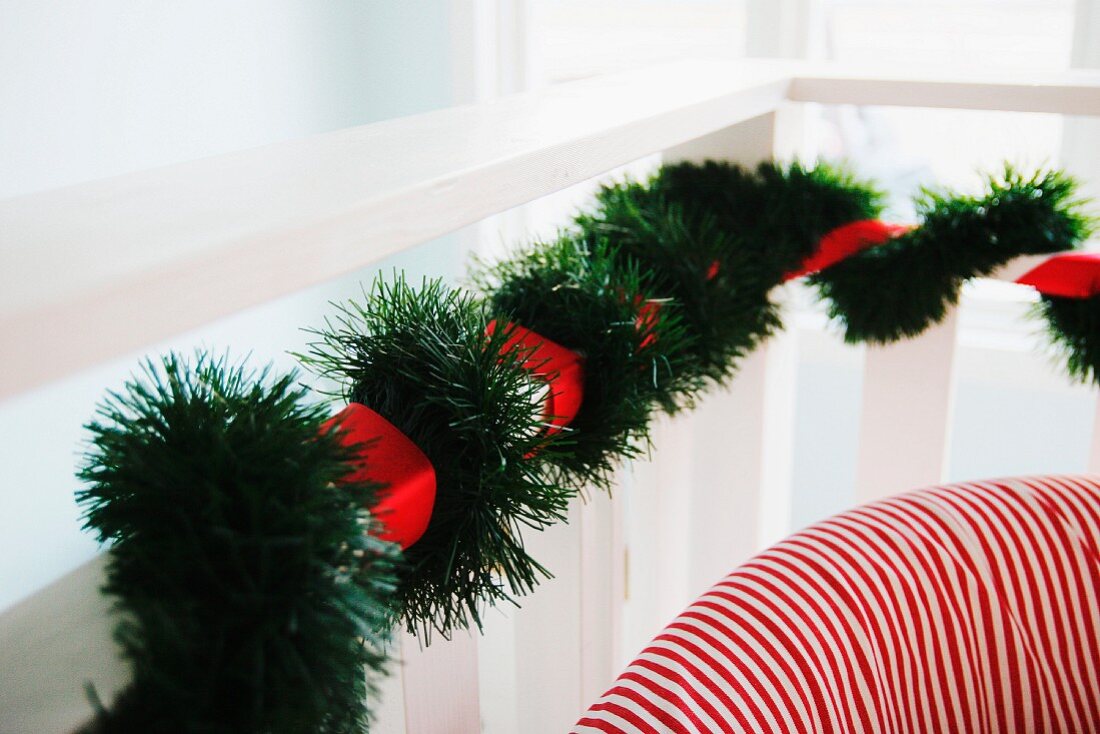 Artificial fir garland and red ribbon wrapped around balustrade and backrest of red and white striped armchair