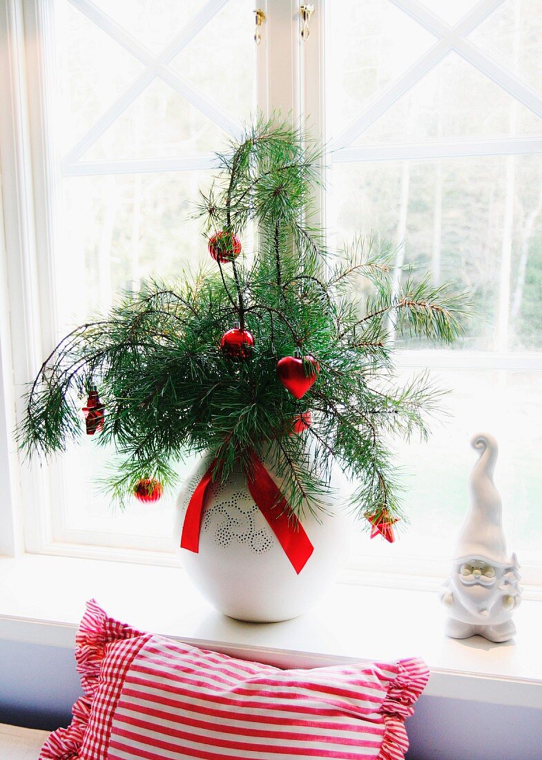 Red Christmas baubles hanging from pine branches in vase and china gnome on windowsill