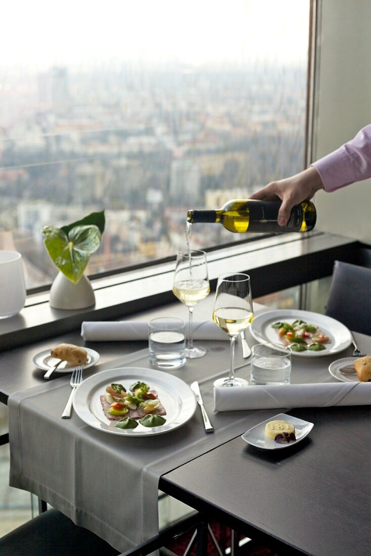 Restauranttisch mit serviertem Tafelspitz vor großem Panoramafenster mit Aussicht auf die Stadt