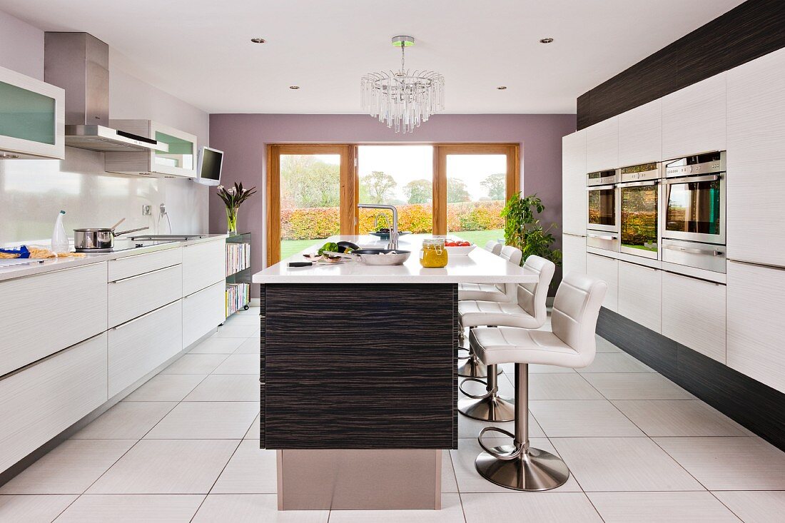 A contemporary kitchen in white with barstools at an island counter on a white tiled floor